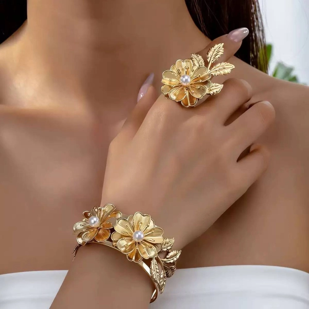 Gold-tone flower cuff bracelet and matching flower ring with pearl centres, worn on a hand